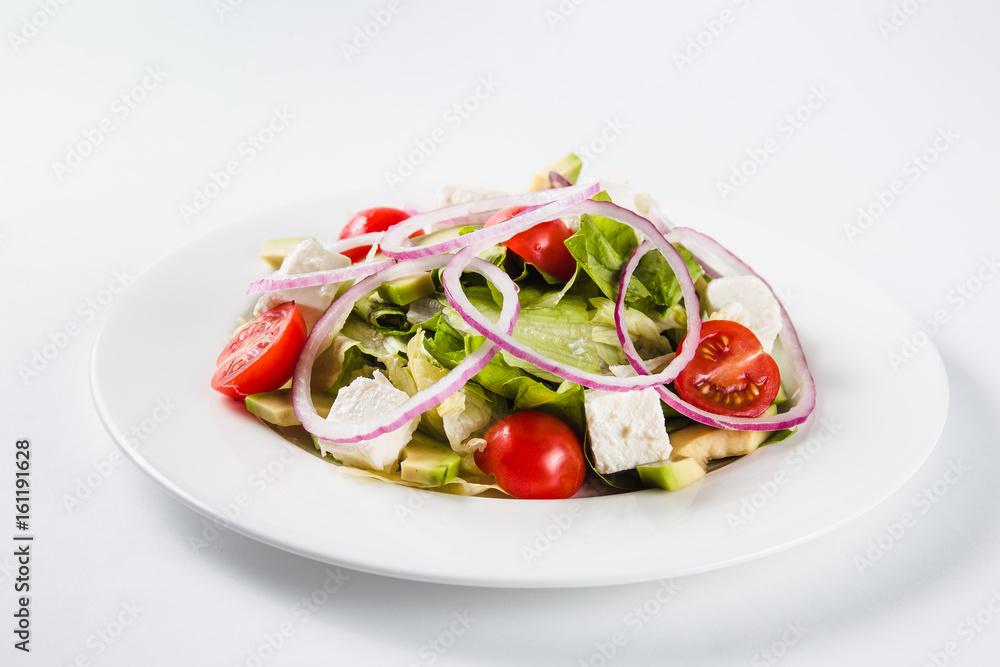 Salad with arugula and tomatoes on a round white plate on a light background (close)