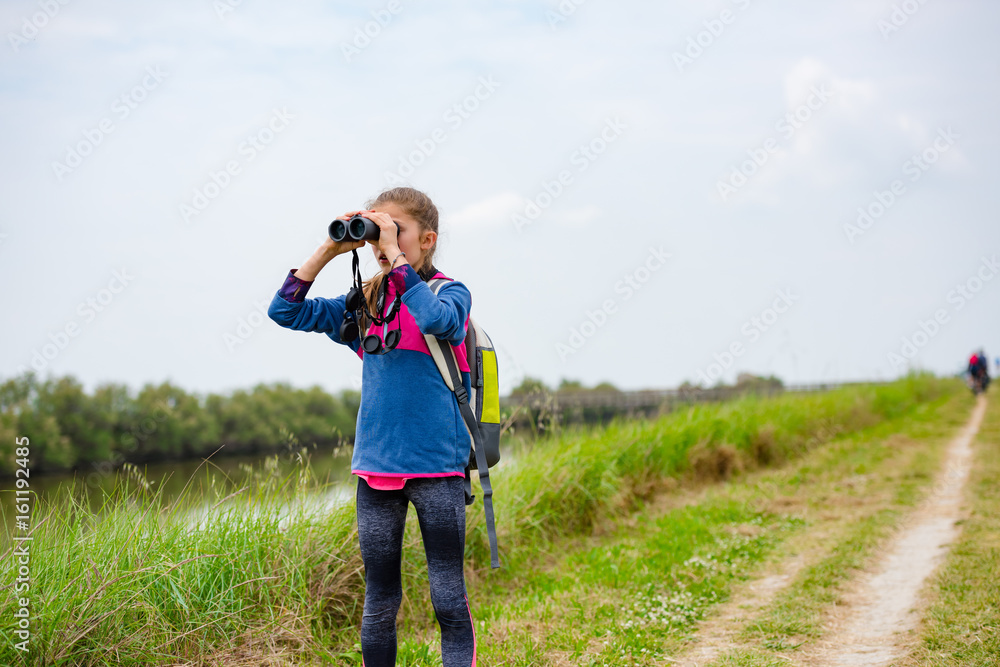 Young girl watching through binoculars on a trail near the river Young girl watching through binoculars on a trail near the river