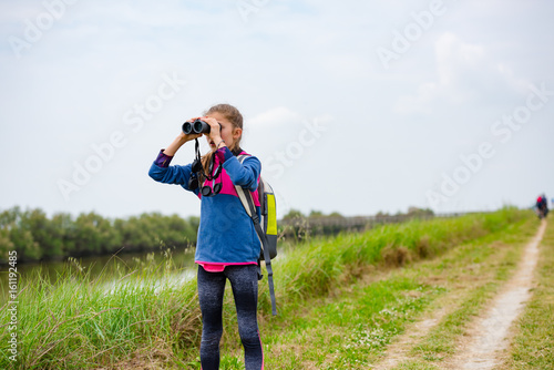 Young girl watching through binoculars on a trail near the river