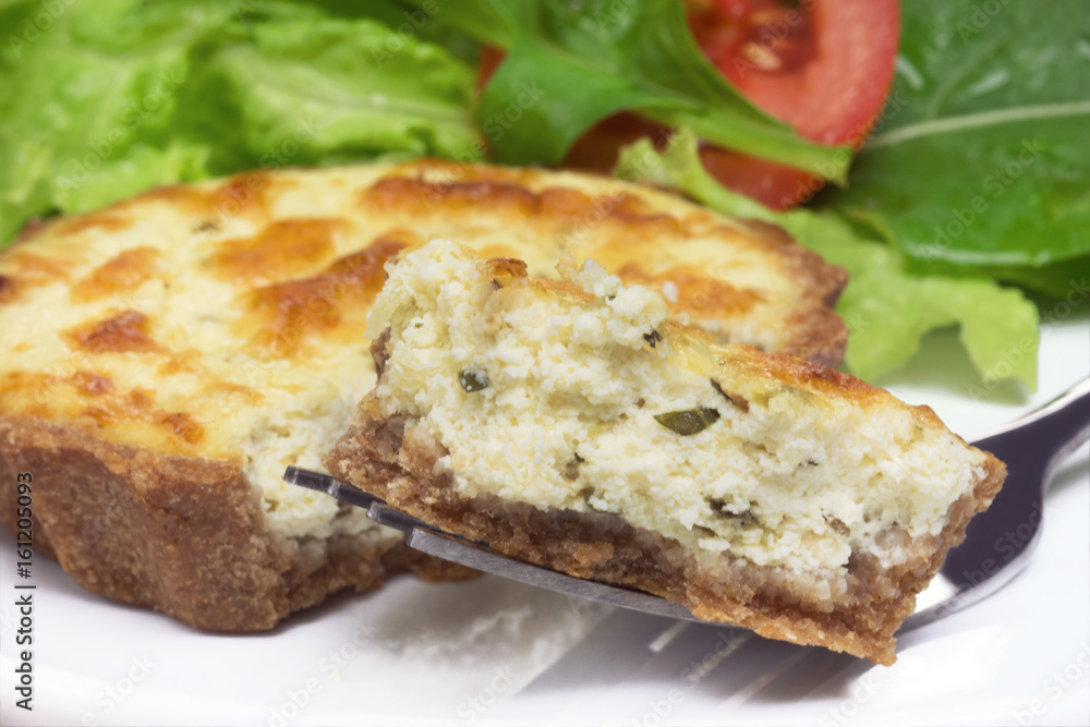 Piece of a mini wholemeal quiche in a fork close with salad in the background Piece of a mini wholemeal quiche in a fork close with salad in the background