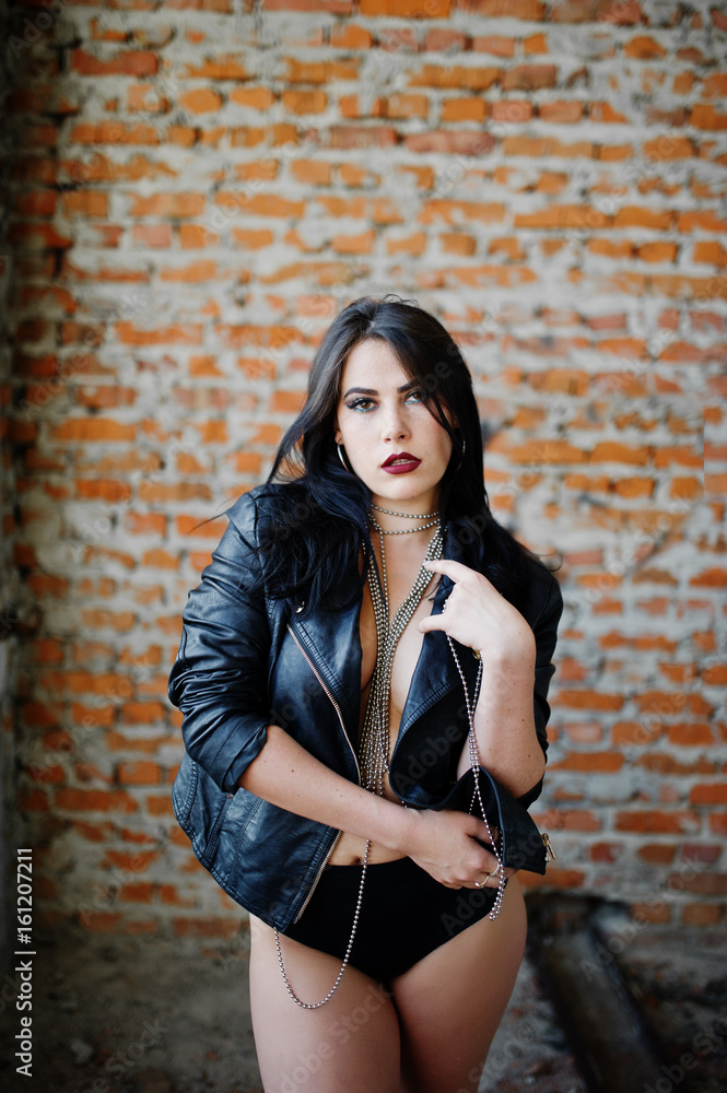 Brunette plus size sexy woman, wear at black leather jacket, lace panties near brick wall at abadoned place. Woman's bare chest.