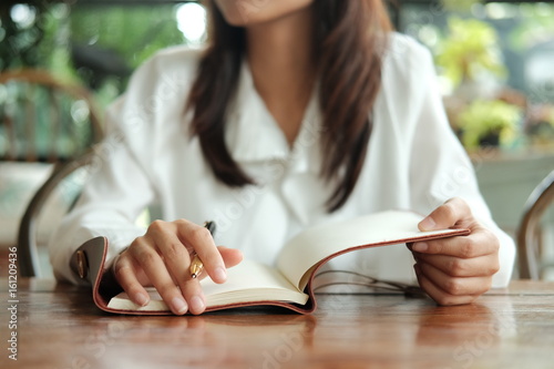 young student woman wearing glasses sitting at library holding pen and writing on notebook paper prepare for exam. image for business,education,book,people and portrait concept
