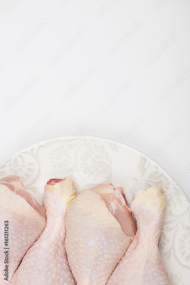 Fototapeta premium Close-up of pile of raw chicken thighs isolated on dish. Copy space. Vertical studio shot.