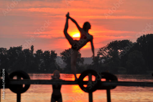 Ein schöner, roter Sonnenuntergang am See, davor macht ein Mädchen einen Skopion, Tanzfigur,  photo