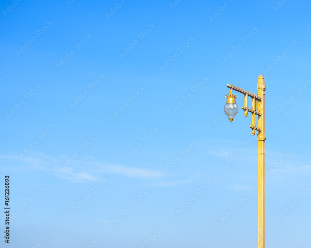 Beautiful design of golden post of public street lamp with blue sky and little white cloud as background. Complementary color. Beautiful design of golden post of public street lamp with blue sky and little white cloud as background. Complementary color.