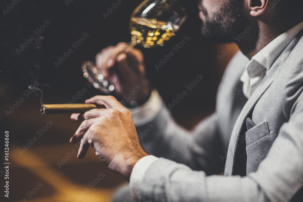 Young man tasting white wine and smoking cigar - obrazy, fototapety, plakaty 