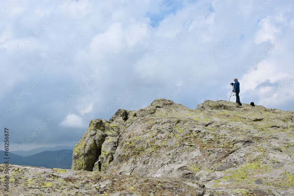Elderly man takes photos with his camera on tripod high on the rocks of Belintash - an ancient Thracian sanctuary with stellar map dedicated to god Sabazios - Dionysus, Rhodope Mountain, Bulgaria