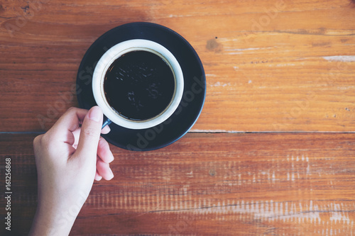 Top view image of a hand holding a cup of hot coffee on wooden table background