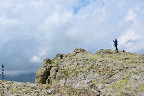 Elderly man takes photos with his camera on tripod high on the rocks of Belintash - an ancient Thracian sanctuary with stellar map dedicated to god Sabazios - Dionysus  Rhodope Mountain  Bulgaria