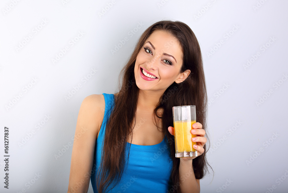 Beautiful happy young healthy casual woman holding the glass with orange juice in the hand on blue background Beautiful happy young healthy casual woman holding the glass with orange juice in the hand on blue background