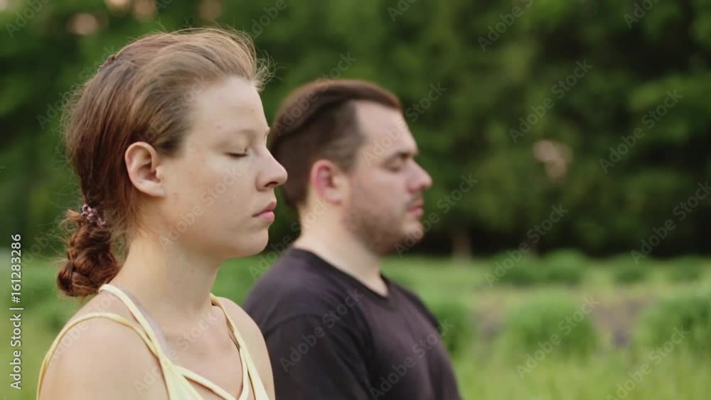 A man and a woman meditate in bliss. Young yoga instructors practice in a city park on green grass. Successful young people perform acro yoga exercises. A man and a woman meditate in bliss. Young yoga instructors practice in a city park on green grass. Successful young people perform acro yoga exercises.