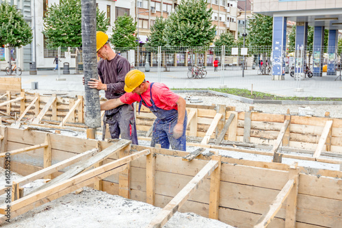 Workers are pouring fresh concrete in vertical wooden mold with hose, continuous casting