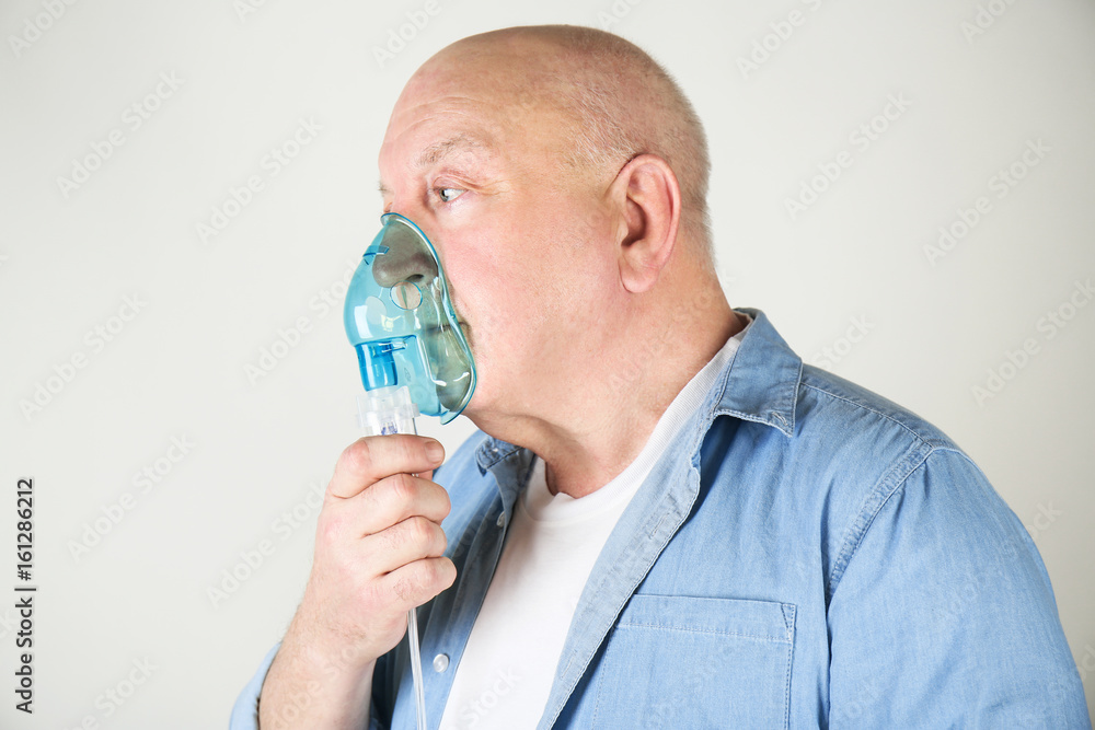 Senior man using asthma machine on light background Senior man using asthma machine on light background