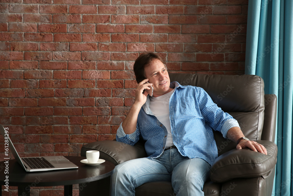 Mature man talking on phone while sitting in armchair Mature man talking on phone while sitting in armchair
