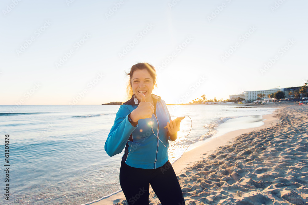 Concept of sport, fitness, healthy lifestyle and running - Motivated sporty woman doing thumbs up success gesture after outdoors workout at the beach Concept of sport, fitness, healthy lifestyle and running - Motivated sporty woman doing thumbs up success gesture after outdoors workout at the beach