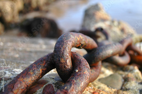 Rusty chain stretching over concrete block at the seaside © sbuwert