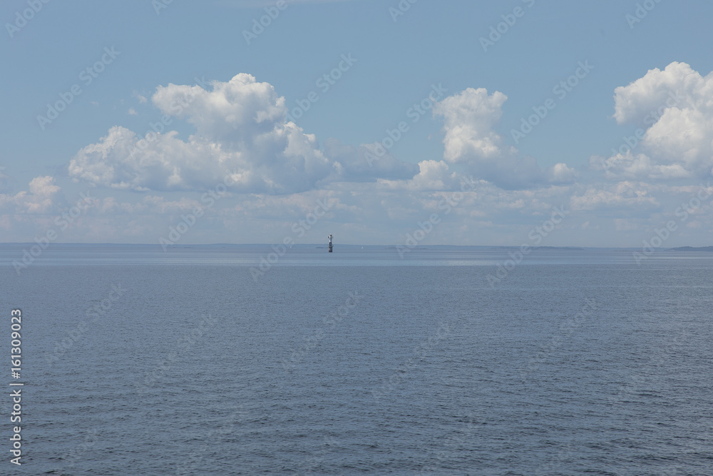 A small lighthouse in the fare end of the sea with some small sailing ships in the background