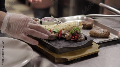 Chef finishing plate and almost ready to serve at table. Only hands finally dish dressing steak meat with green parsley. Meat on skewers, decorated with greens, pita bread, salad with vegetables, on photo