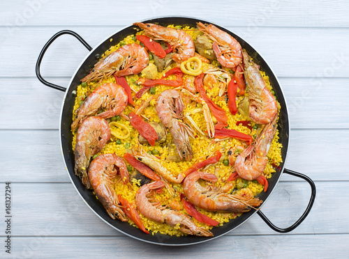 From above big paella dish containing shrimps and rice with vegetables.