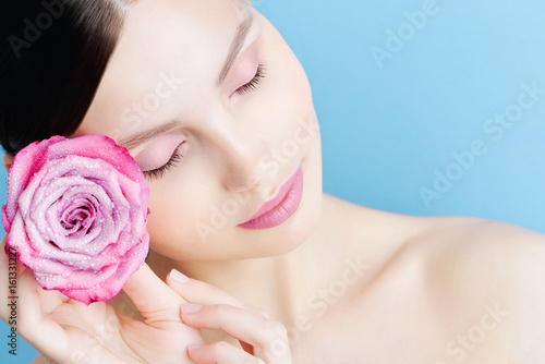 Portrait of a beautiful brunette girl with a pink rose on a blue background