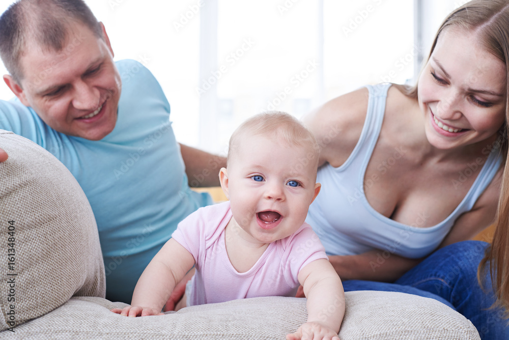 Joyful child crawling on sofa and happy parents looking at it Joyful child crawling on sofa and happy parents looking at it