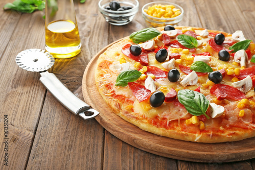 Plate with tasty pizza, its ingredients and knife on wooden table