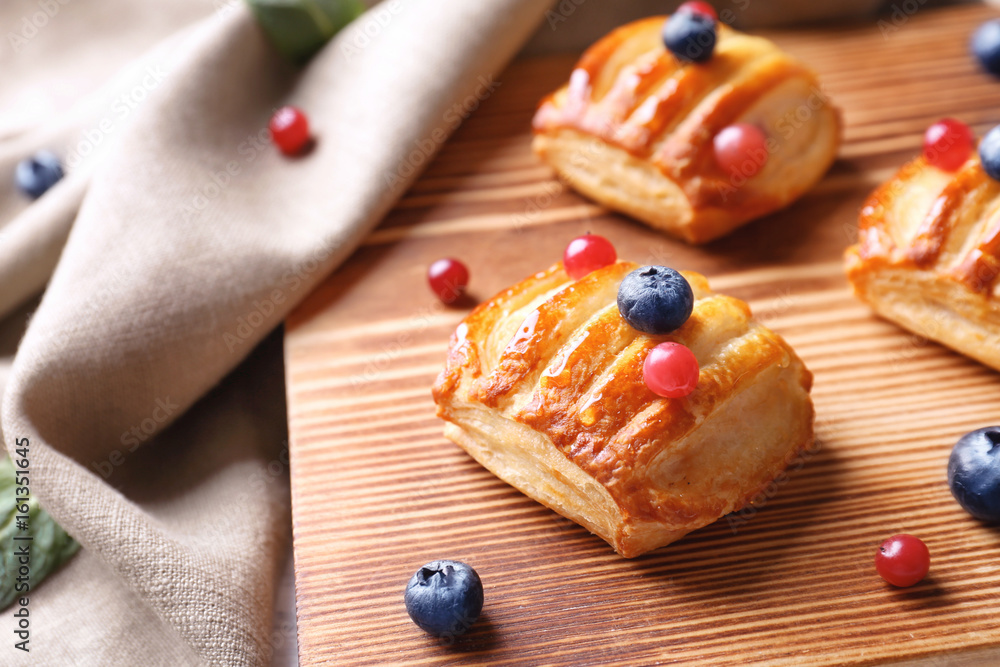Delicious pastries with berries on cutting board, closeup