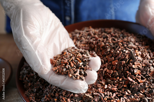 Human hand in glove taking pile of cocoa nibs from plate