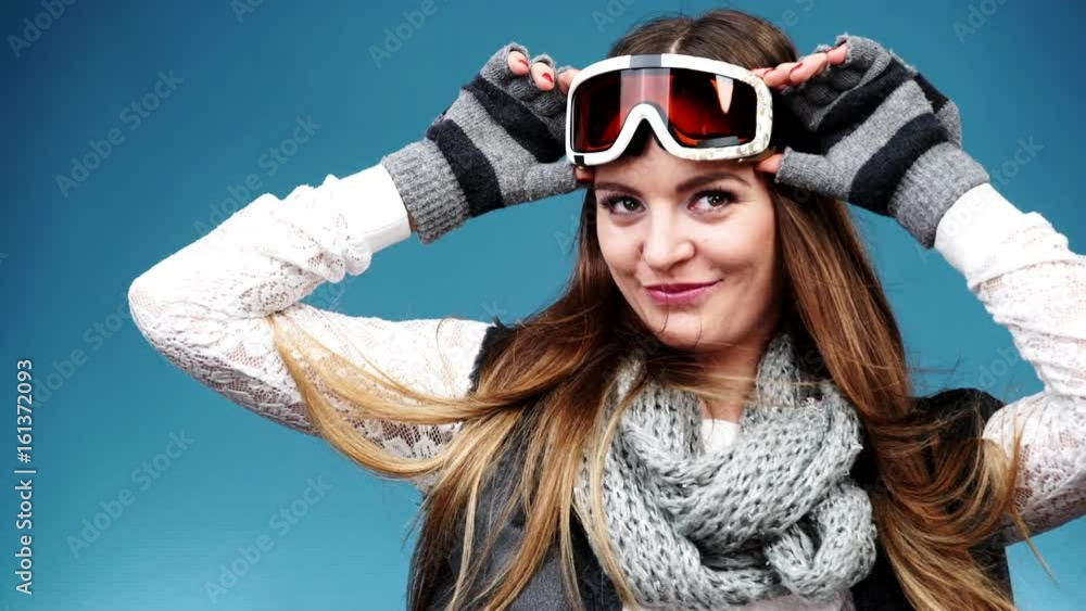 Woman smiling skier girl wearing warm clothing ski goggles portrait. Winter sport activity. Beautiful long hair sportswoman on blue studio shot, full HD. Woman smiling skier girl wearing warm clothing ski goggles portrait. Winter sport activity. Beautiful long hair sportswoman on blue studio shot, full HD.