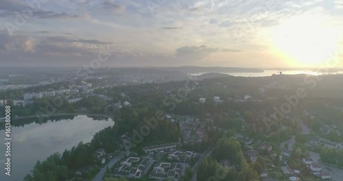 Late evening aerial view of city, forest, lakes, cumulus clouds, watertower and sunset in Lahti, Finland, sideways movement