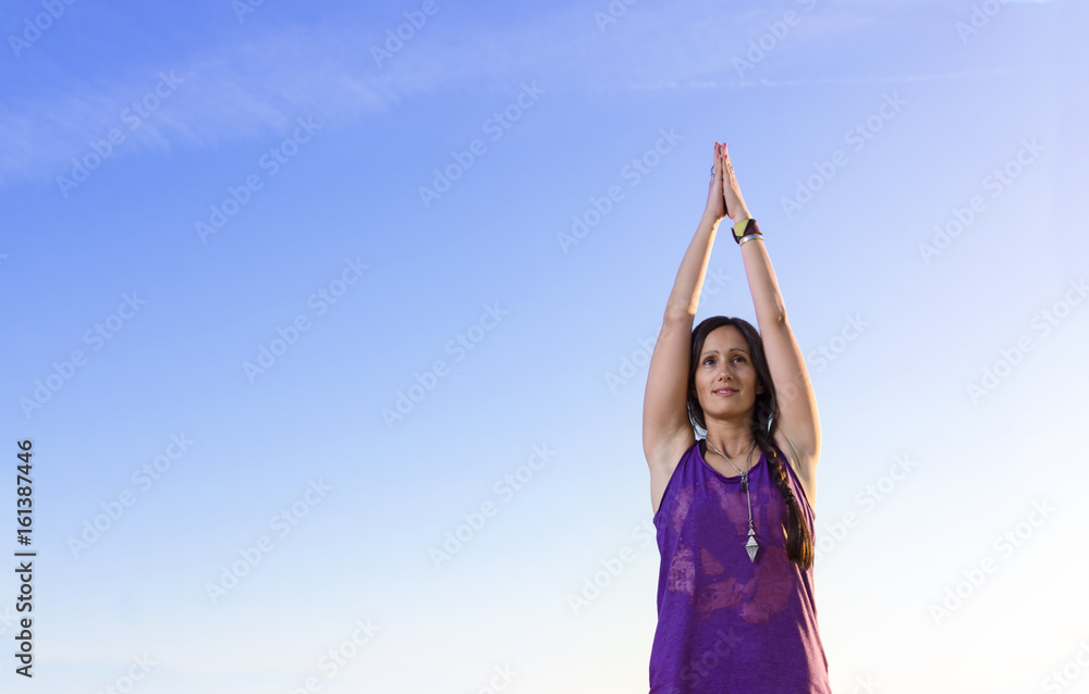 Closeup of beautiful young woman in yoga prayer pose, copy space on blue sky