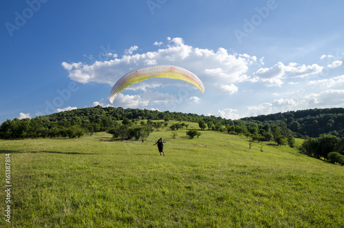 Man with paraglider on green grass field, getting ready for the takeoff 