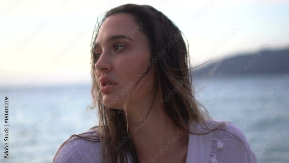 Closeup portrait of sensual woman in white linen dress posing on the sandy beach on tropical paradise island with beatiful summer sunset sky - video in slow motion