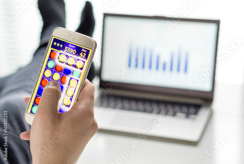 Lazy office worker playing mobile game with smartphone during work hours. Avoiding his job and being lazy with feet and socks on table. Useless and unproductive man doing nothing and forget his job. photo