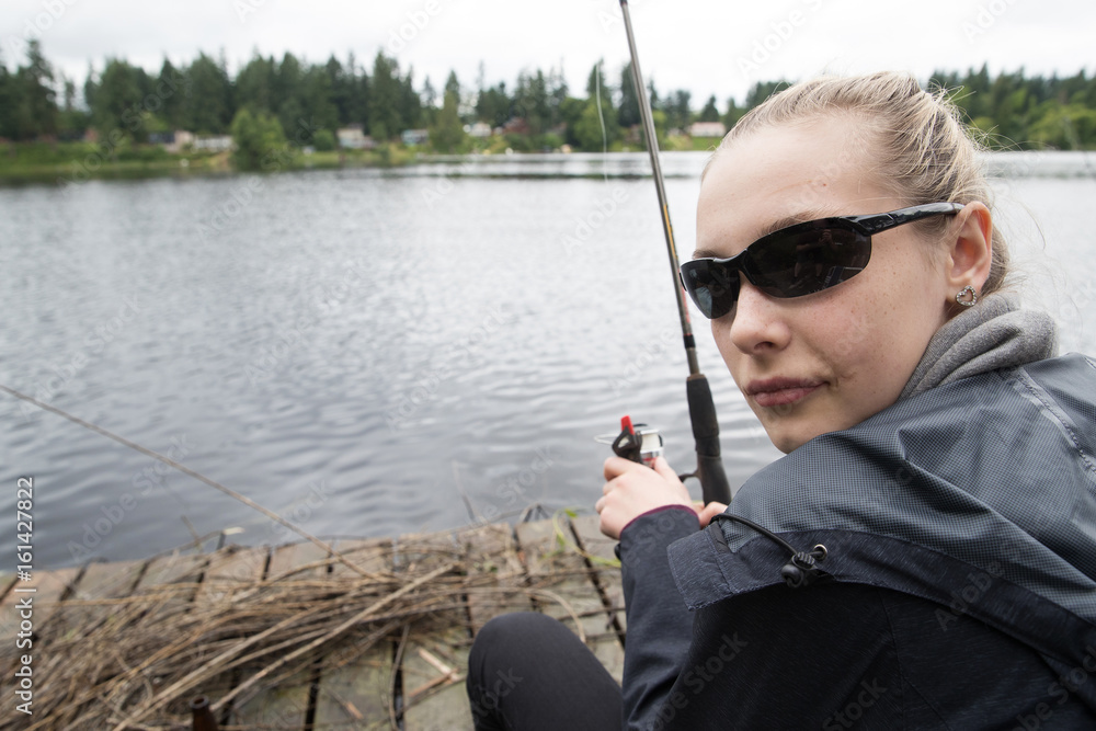 Teenage girl fishing in a lake while sitting on a dock Stock Photo