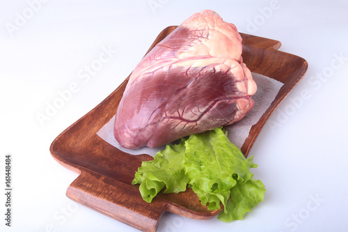 Raw beef heart and lettuce leaf on wooden desk isolated on white background from above and copy space. ready for cooking.