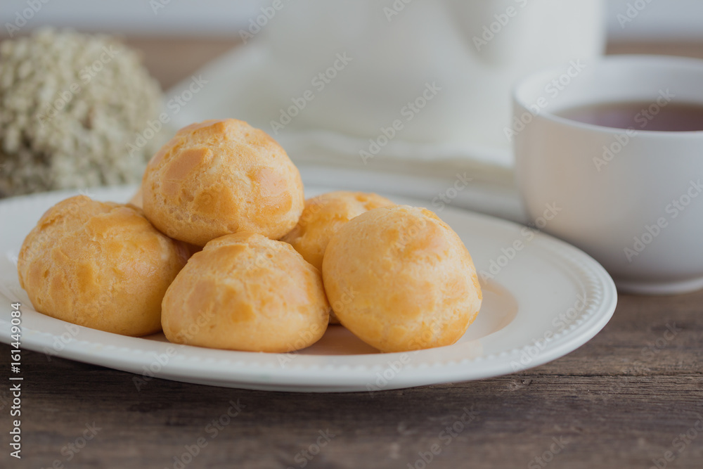 Homemade cream puffs filled with vanilla custard cream. Cream puffs or choux or eclairs in white plate on rustic wood table. Golden choux pastry for coffee break or tea time. Natural tone style. Homemade cream puffs filled with vanilla custard cream. Cream puffs or choux or eclairs in white plate on rustic wood table. Golden choux pastry for coffee break or tea time. Natural tone style.