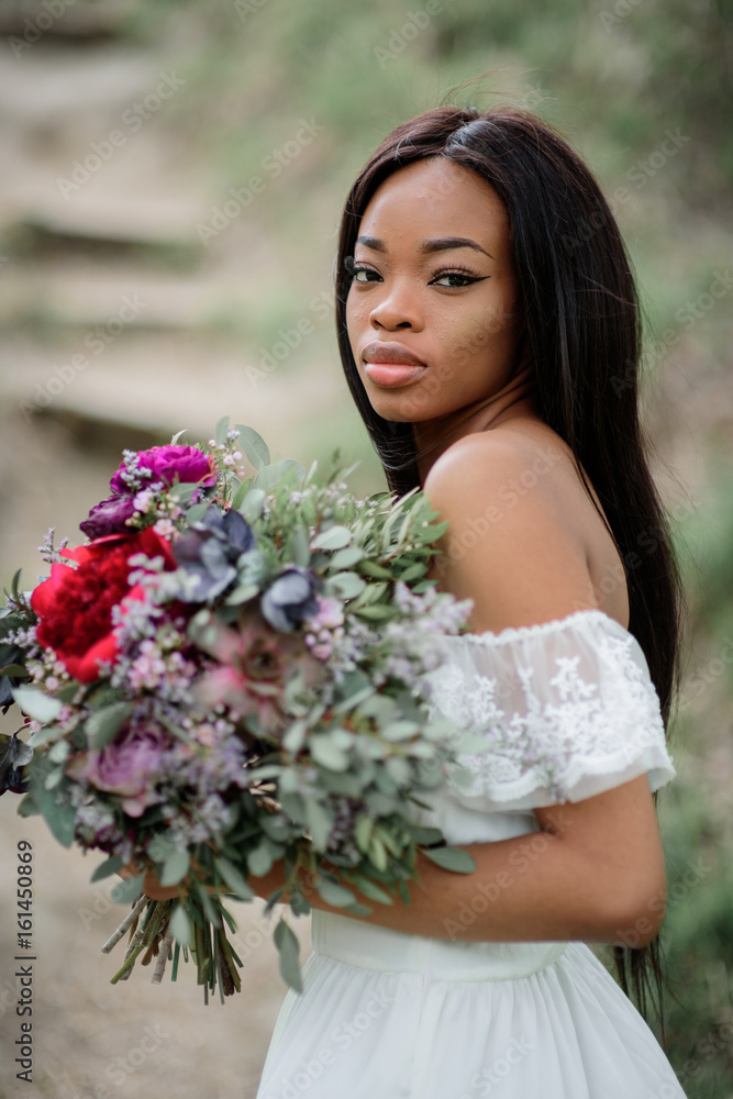 Bride with dark skin holds rich red bouquet in her tender arms Bride with dark skin holds rich red bouquet in her tender arms