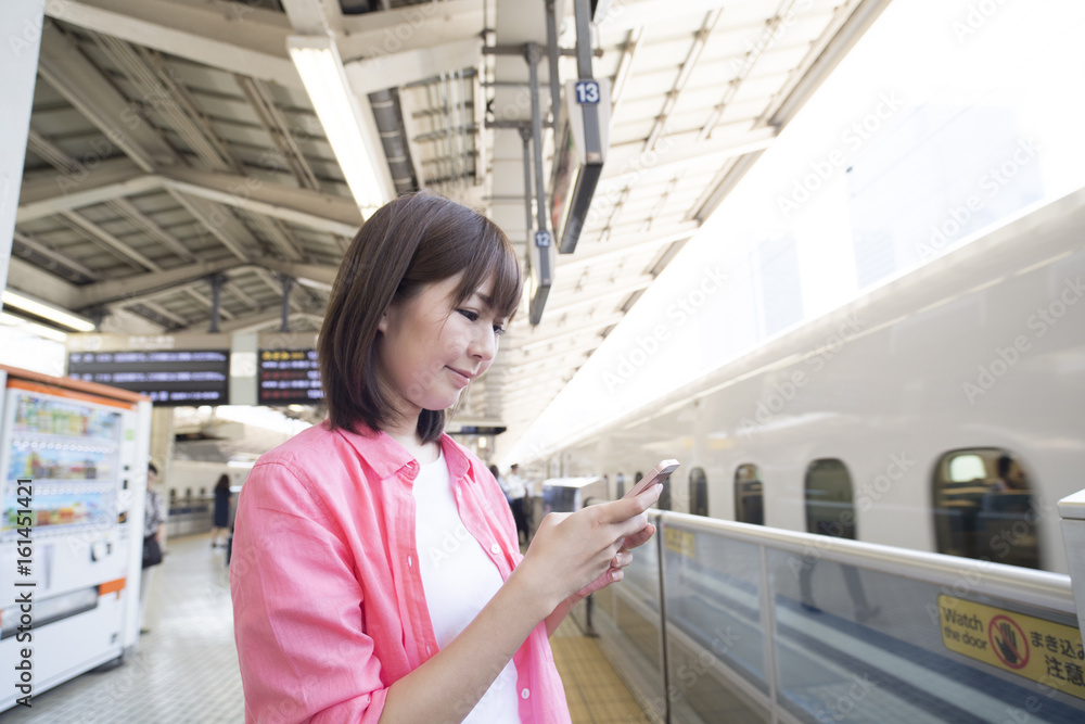 Naklejka premium A woman is waiting for a bullet train while watching a smartphone
