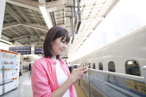 A woman is waiting for a bullet train while watching a smartphone