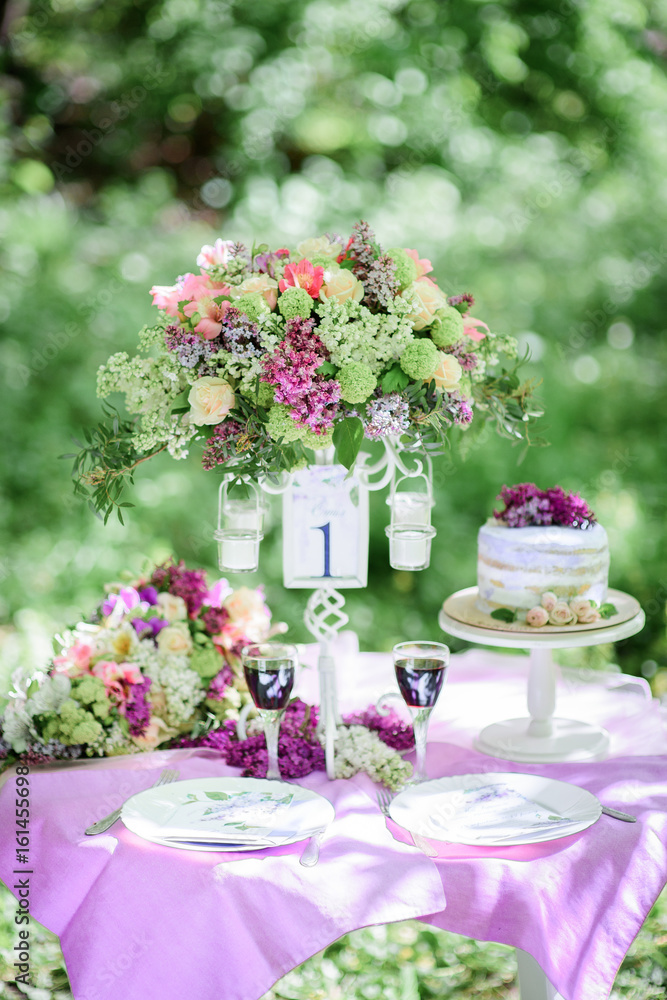 Table number one with bouquet of violet flowers and little cake on it stands in the garden