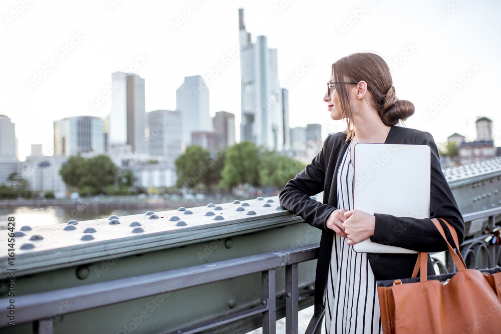 Portrait of a young businesswoman with laptop standing on the bridge in Frankfurt city Portrait of a young businesswoman with laptop standing on the bridge in Frankfurt city