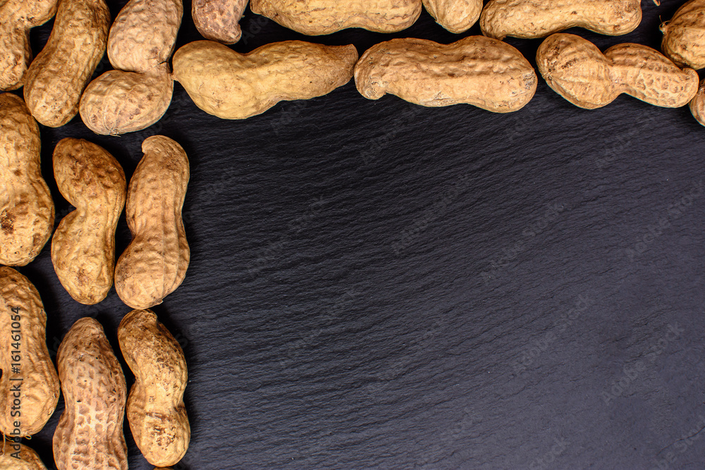 Fototapeta premium Unclean peanuts lie on a black stone board in the form of a frame, space for text