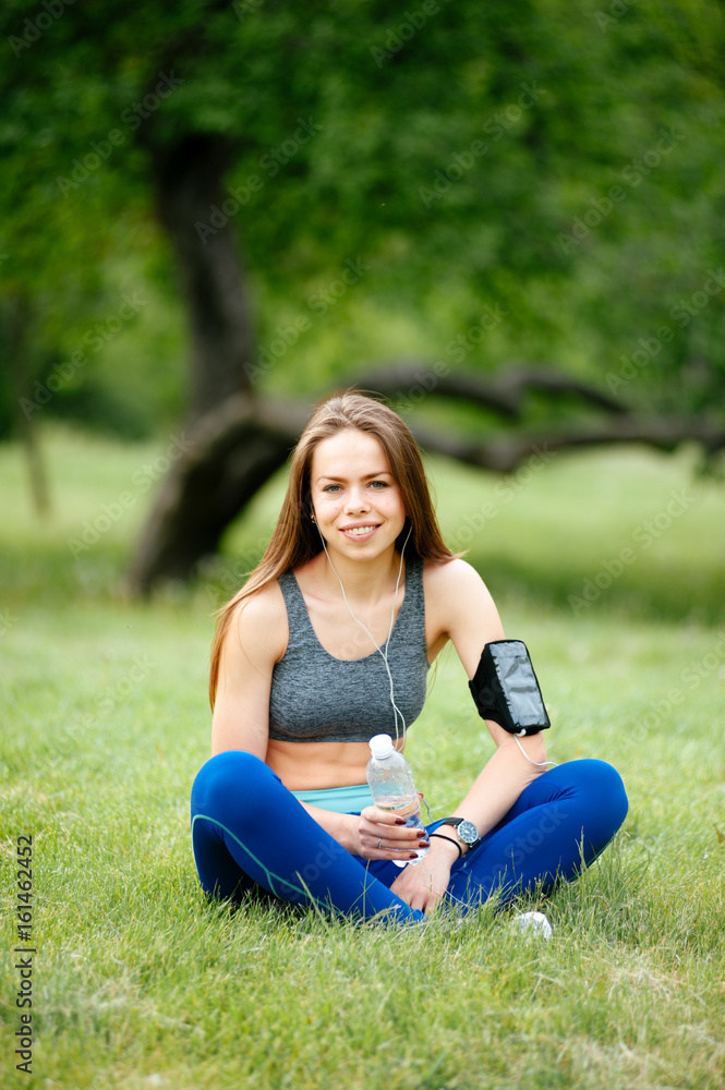 Happy sporty woman in headphones outdoors in park. Attractive sporty girl is listening to music using smartphone. Happy sporty woman in headphones outdoors in park. Attractive sporty girl is listening to music using smartphone.