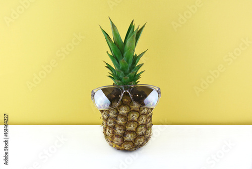 Ripe pineapple wearing sunglasses on yellow background.