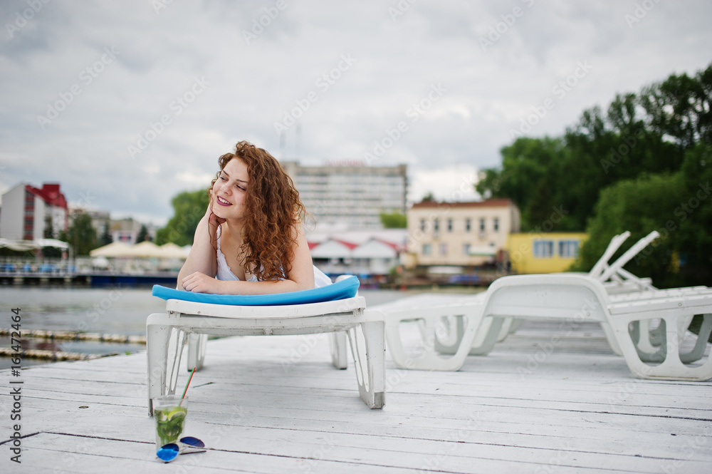 Portrait of a very beautiful girl laying and posing on a launger on a lakeside.