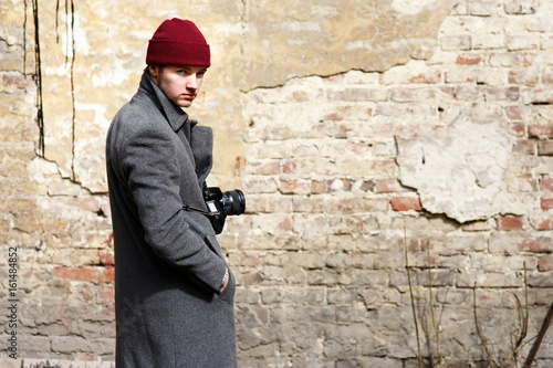 Man with camera on his neck stands before old ruined wall