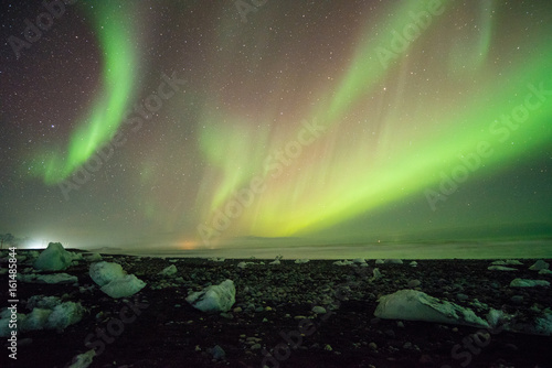 aurora borealis over black sand beach and ice cubes, iceland.
