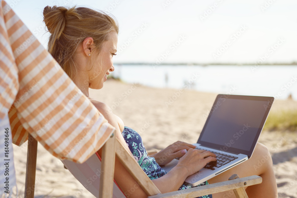 Young woman typing on a laptop on a beach