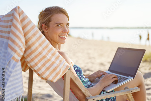 Friendly young woman using a laptop at the beach